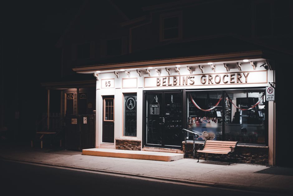 Nighttime view of Belbin's Grocery storefront with warm lighting and an inviting bench.