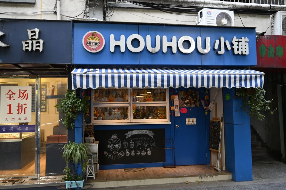 Charming storefront with a blue facade and striped awning, featuring playful signage and plants.