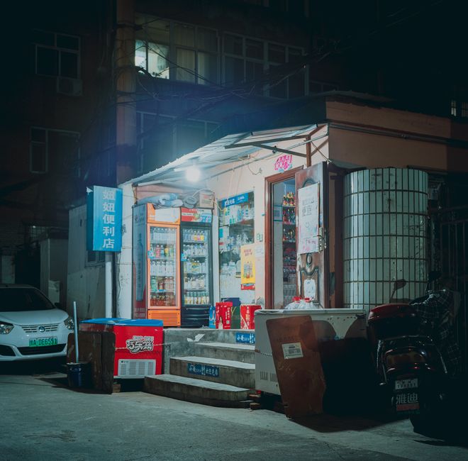 A small illuminated corner store on an urban street at night with visible goods.
